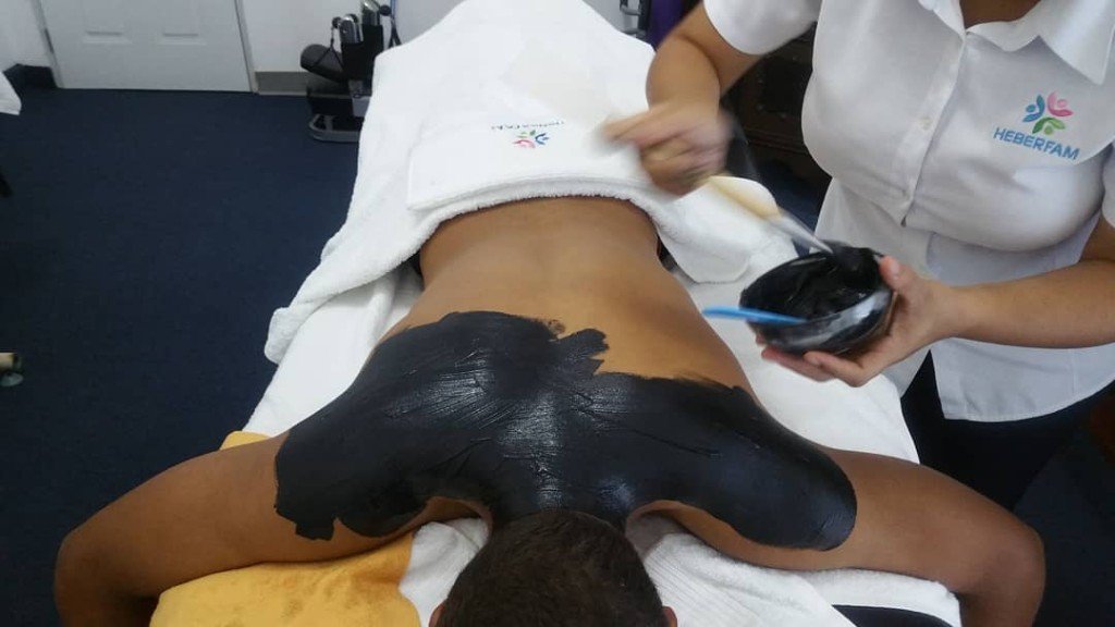 Aplicación de fango negro sobre la espalda de un paciente